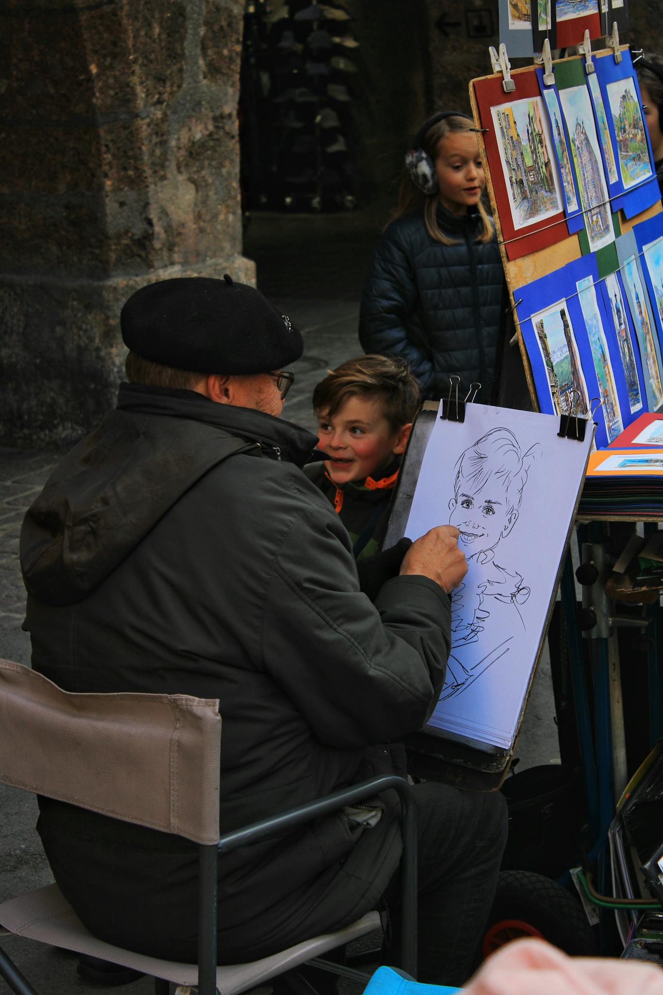 A street artist sketches a smiling child outdoors in Innsbruck, Austria.