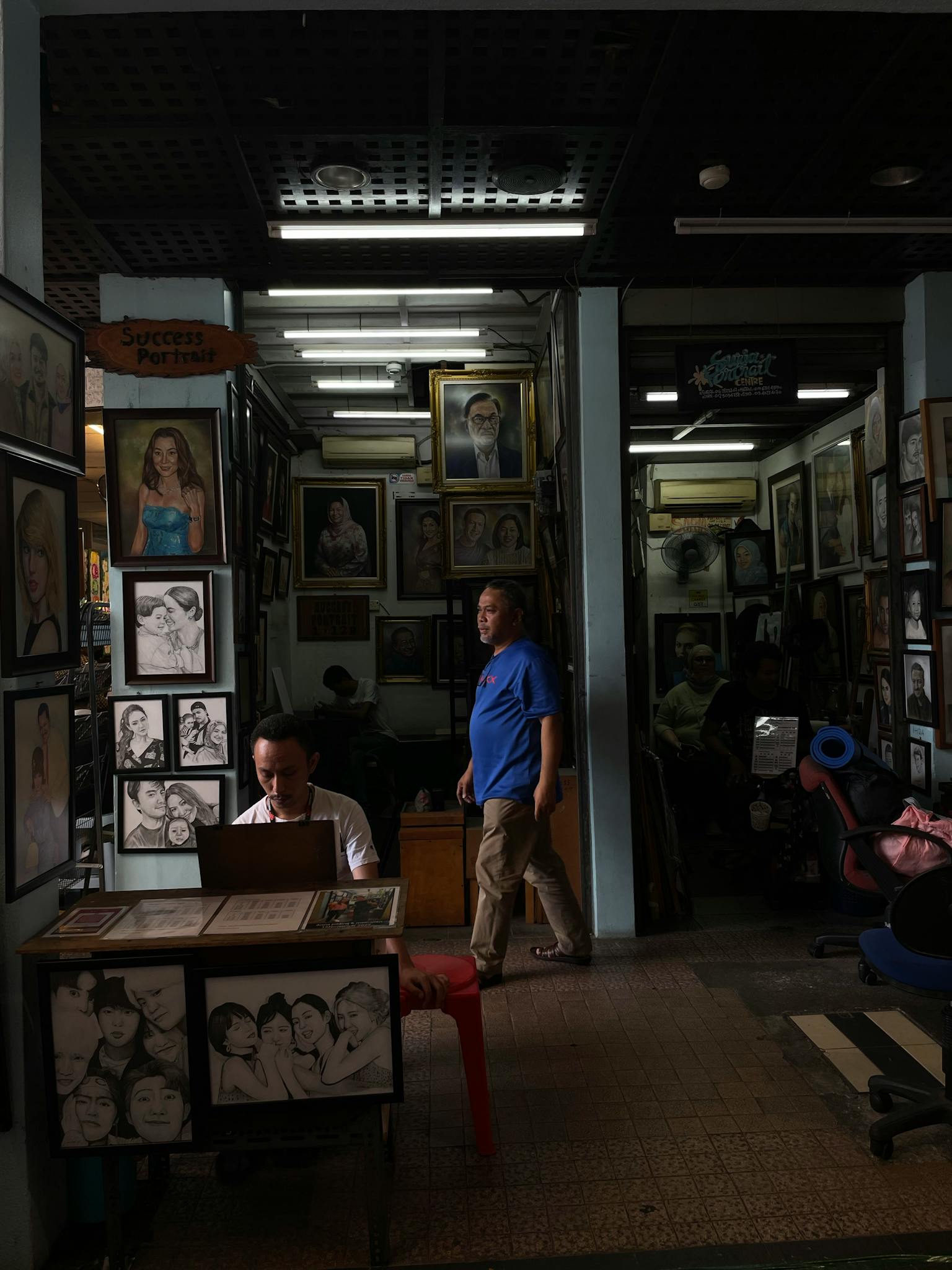 An art shop bustling with portraits and activity, showcasing diverse artwork indoors.