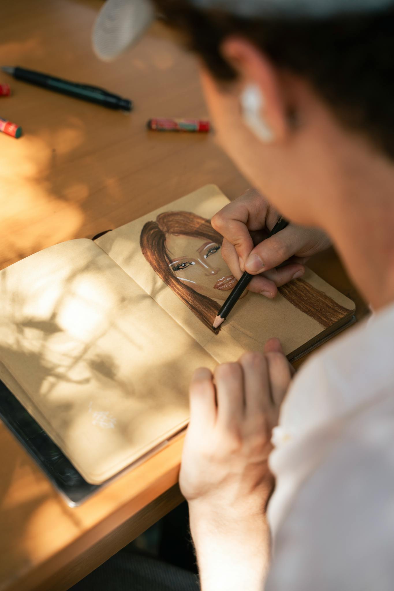 Close-up of an artist drawing a female portrait with pencils in a sketchbook during daytime.